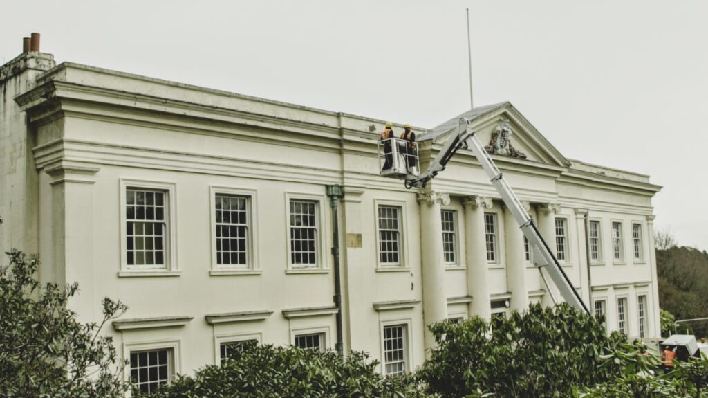 Workers in an elevated platform clean windows of a grand historic building with white façade.